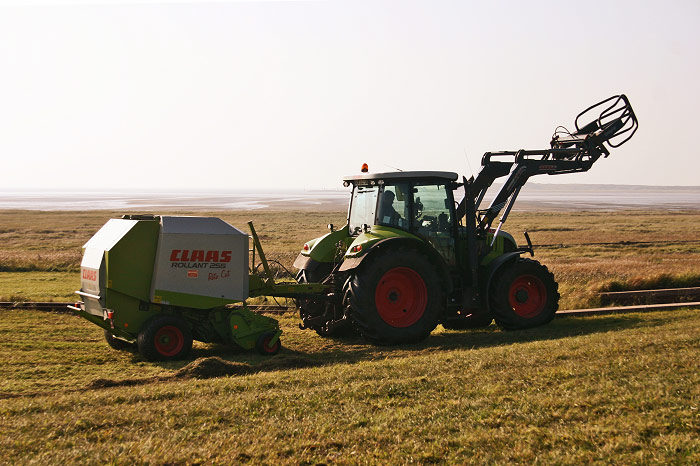 Traktor mit Rundballenpresse am Deich